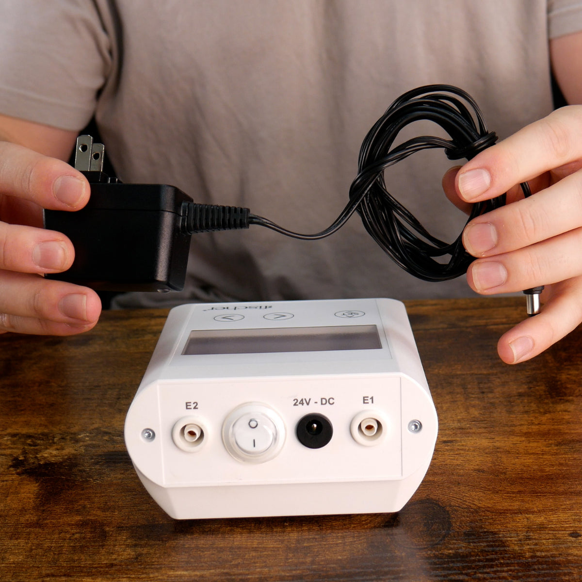 A person holding the power cord for the Fischer iontophoresis device, used to treat hyperhidrosis (excessive sweating), next to the Fischer main control unit 